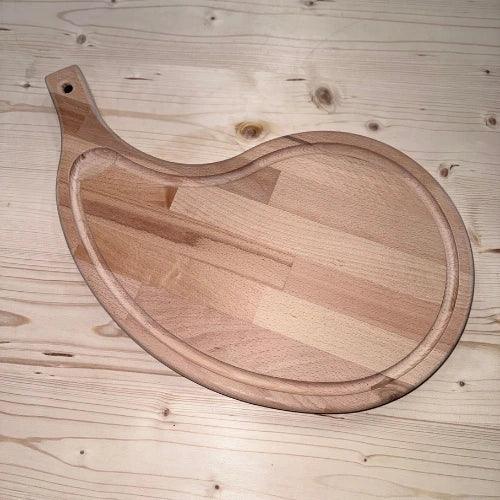 Planche à découper en bois massif en forme originale sur fond de table en bois clair.