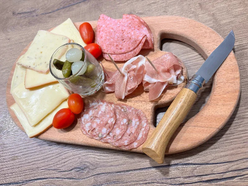 Planche à découper en bois massif garnie de fromage, charcuterie, tomates et cornichons.
