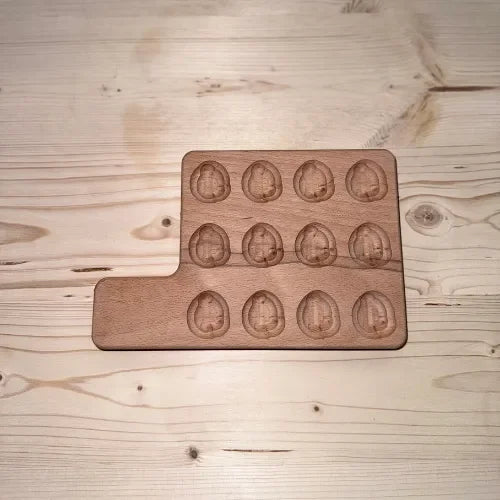 Planche en bois massif avec 12 emplacements ovoïdes gravés, posée sur une table claire.