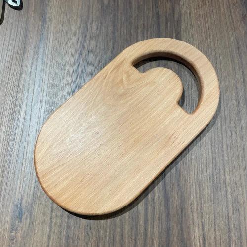 Planche à découper en bois massif ovale avec poignée, posée sur une table en bois