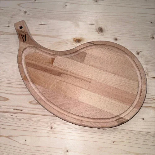 Planche à découper en bois massif en forme originale, posée sur une table en bois clair.
